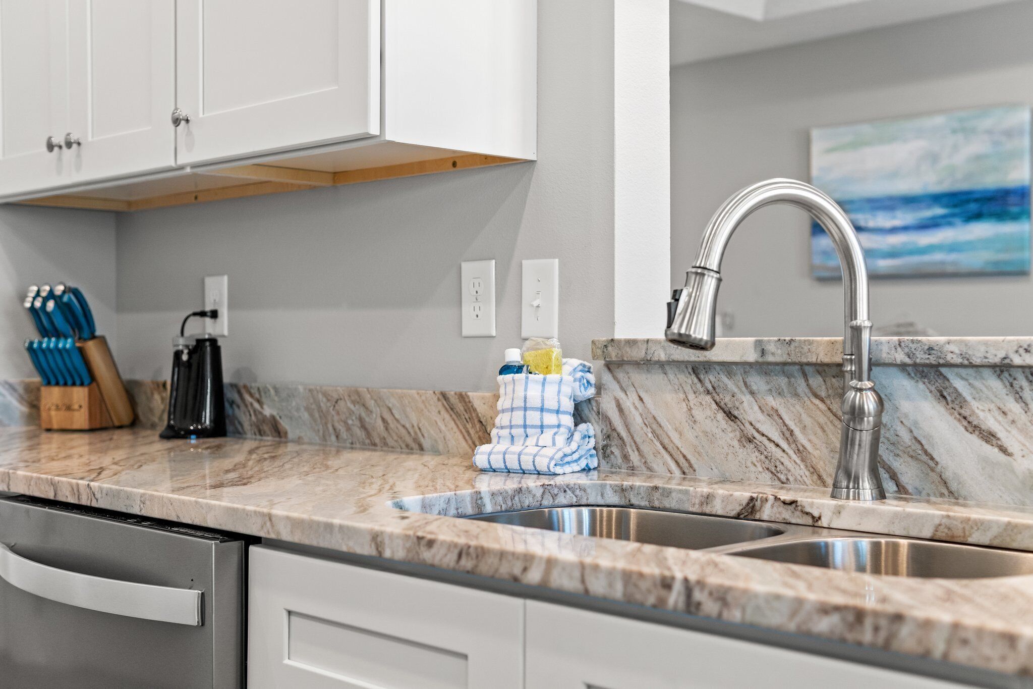A kitchen with a marble countertop, stainless steel sink, and white cabinets.