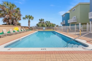 A swimming pool with a 3 FT depth marker, surrounded by a white fence, palm trees, and a building with balconies.