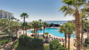 Un resort con una amplia piscina rodeada de palmeras y sillas de descanso, con vistas al océano.
