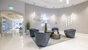 A modern reception area with a curved wall, a sign reading "The Club at Brickell Bay Condominium," and a reception desk with a lamp and seating area. - Brickell Home with New Floors & Kitchen 41st Floor (Miami)