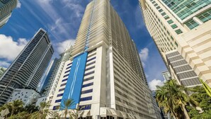 A high-rise building with a prominent blue stripe, surrounded by other tall buildings and palm trees. - Brickell Home with New Floors & Kitchen 41st Floor (Miami)