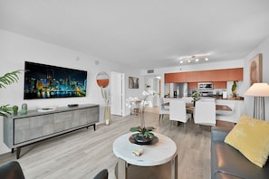A modern living room with a dining area, a kitchen, and a large cityscape painting on the wall.
