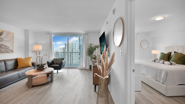 A modern living room with a sofa, coffee table, and a view of the city through large windows. - Brickell Home with New Floors & Kitchen 41st Floor (Miami)
