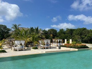 A resort pool area with sun loungers and cabanas, surrounded by palm trees and a clear sky. - Casa privada en la Isla Barú (Cartagena)