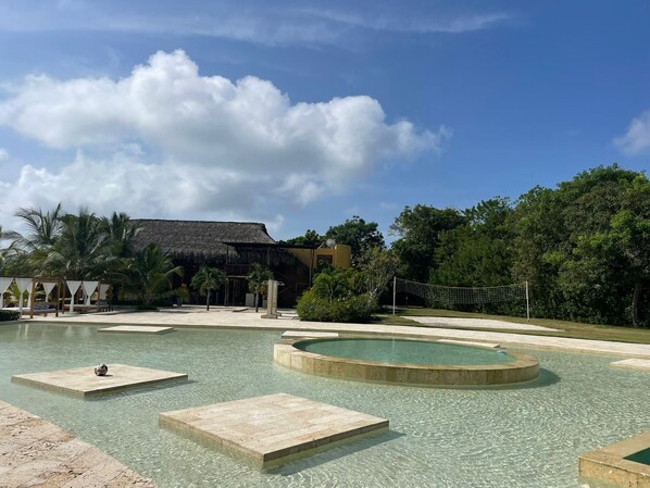 A clear swimming pool with a thatched-roof structure and palm trees in the background. - Casa privada en la Isla Barú (Cartagena)