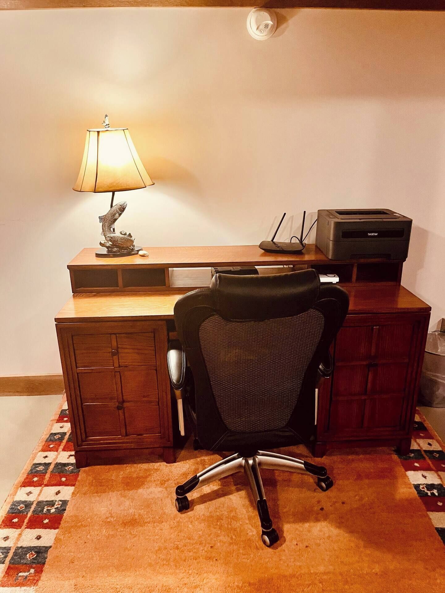 A wooden desk with a lamp, a printer, and a chair.