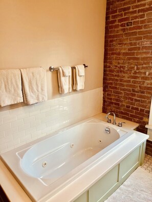 A bathroom with a large bathtub, white tiled walls, and a brick accent wall. - Historical Charm with Modern Comforts (Livingston)