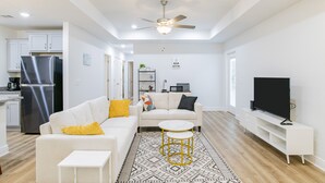 Una sala de estar moderna con un sofá blanco, almohadas amarillas, una mesa de centro y un televisor sobre un mueble blanco.