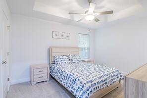 A bedroom with a bed, nightstands, a ceiling fan, a window, and a door.