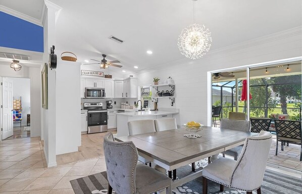 A modern kitchen with white cabinetry, a central island, and a dining area with a large table and chairs.