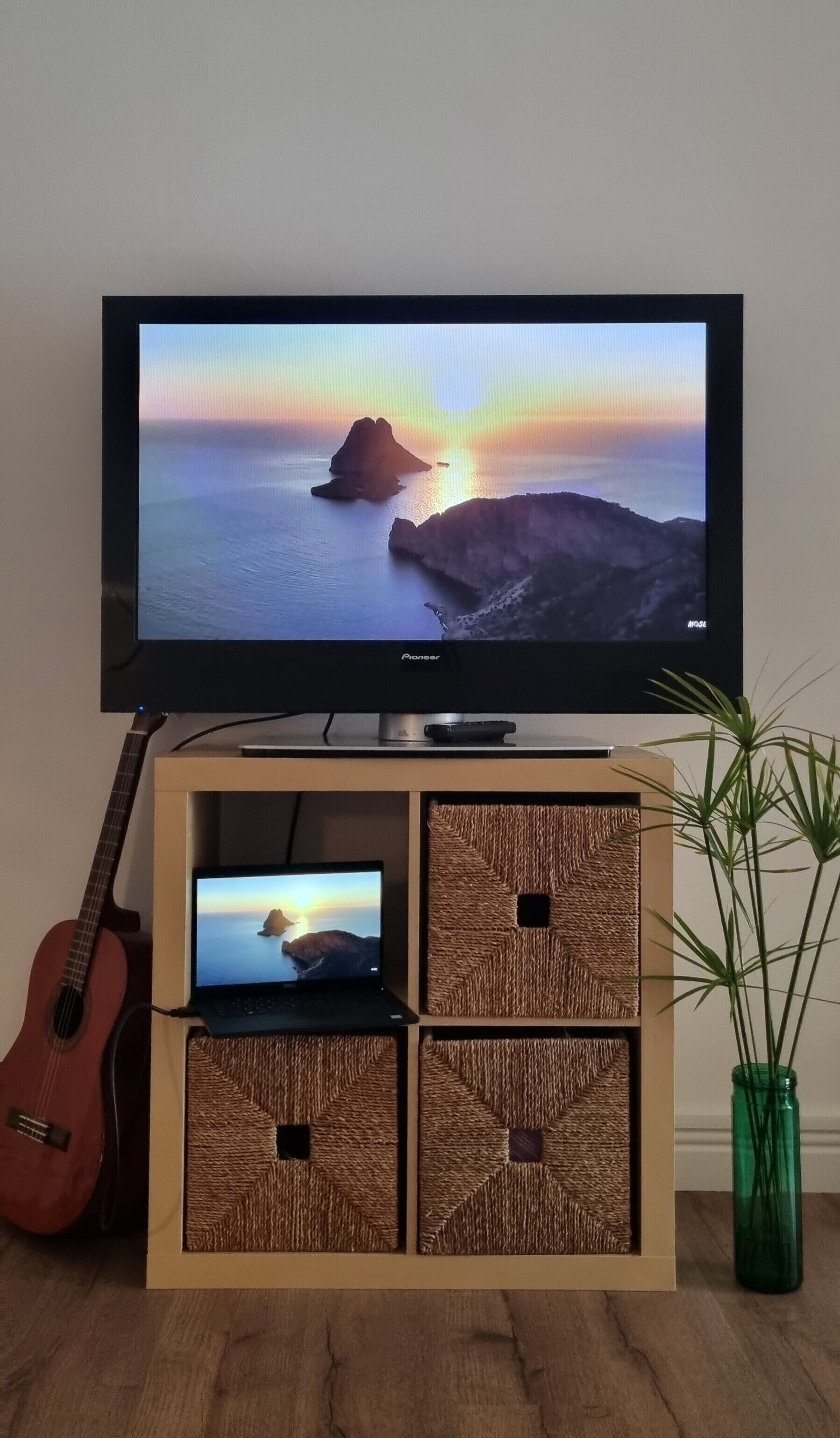 Een televisie op een houten standaard, samen met een gitaar en een laptop.