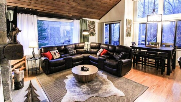 A cozy living room with a sectional sofa, a wooden coffee table, and a large window offering a view of the outdoors. - Loon Outlook - Best View, <3min to Loon (Lincoln)
