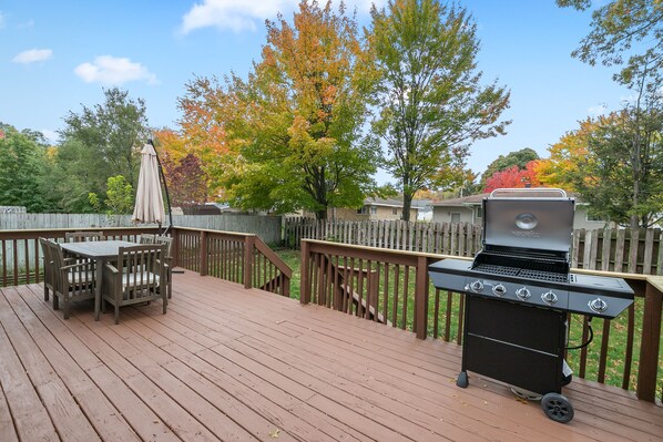 Une terrasse en bois avec un barbecue, une table et des chaises.