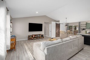Un salon moderne avec un grand canapé gris, un téléviseur à écran plat fixé au mur et une table basse en bois.