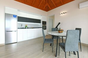 A modern kitchen with white cabinets, a stainless steel refrigerator, and a dining area with a round table and grey chairs.