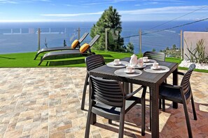 Um pátio com uma mesa posta para dois, com vista para a paisagem deslumbrante do oceano.