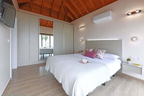 A bedroom with a large bed, a TV mounted on the wall, and an air conditioning unit.