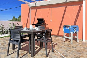 An outdoor patio with a table set for four, a grill, and a blue water dispenser.