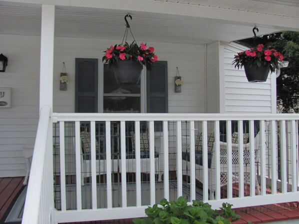 A white porch with a railing, potted plants, and a window with shutters.