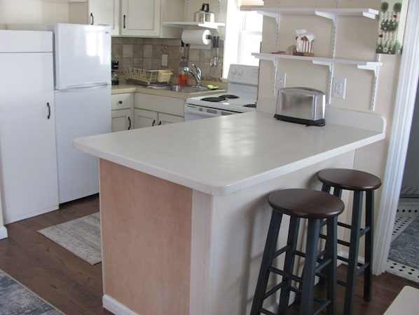 A kitchen with white cabinets, a white refrigerator, a stove, and two bar stools.