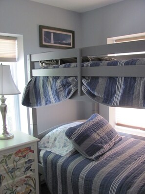A bunk bed with striped bedding, a bedside table with a lamp, and a framed picture on the wall.