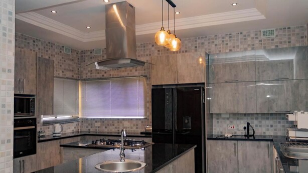 A modern kitchen with a central island, stainless steel appliances, and a large window with blinds.