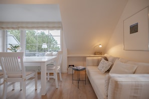 Un salon chaleureux avec un canapé blanc, une table à manger entourée de chaises et une petite table d’appoint avec une lampe.