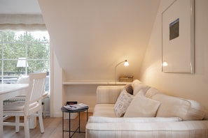Una habitación acogedora con un sofá blanco, una mesa de comedor con sillas, una lámpara y un cuadro en la pared.