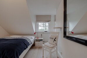 Une chambre à coucher avec un lit, une table de chevet, une chaise, une fenêtre et un miroir.