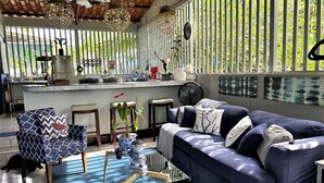 A living room with a blue sofa, patterned armchair, and a glass coffee table. - Casa Sophia (Guapiles)