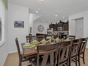 Un coin repas avec une table ronde dressée pour six personnes, entourée de chaises en bois foncé.