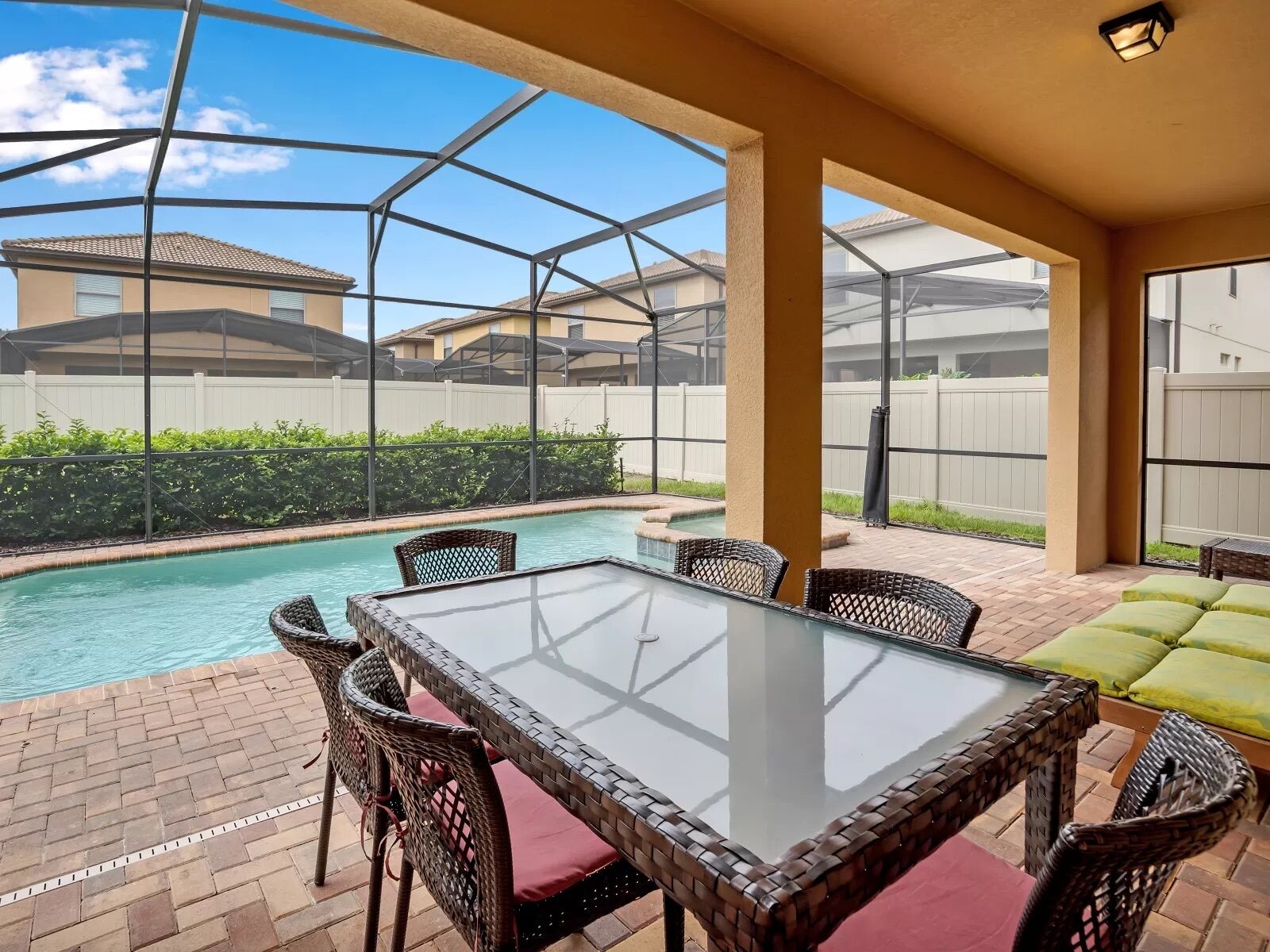 A covered outdoor area with a pool, wicker furniture, and a view of neighboring houses.