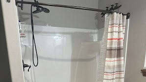 Valkoinen suihkukaappi, punainen ovimatto ja puinen pesuallas, jossa on laatikoita.
