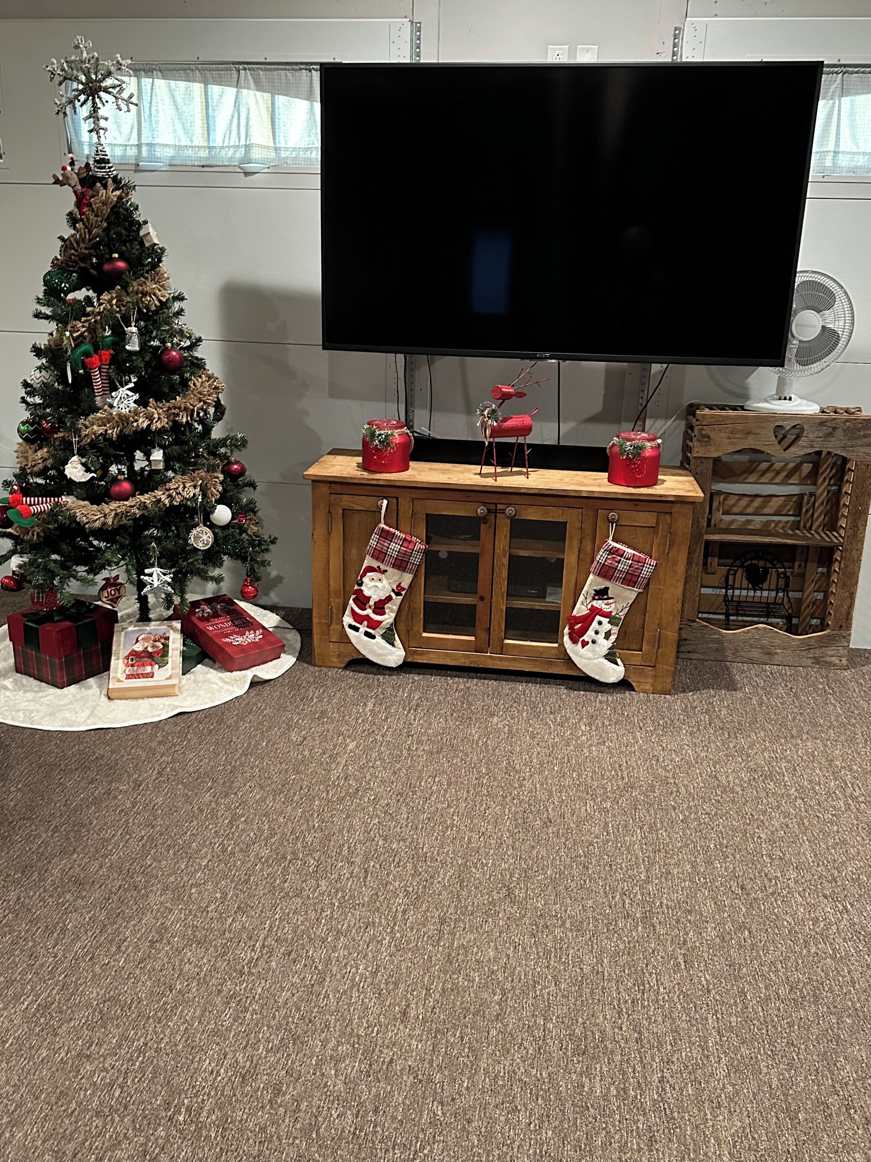 Una sala de estar con un árbol de Navidad, un televisor de pantalla plana y un mueble de madera con calcetines navideños.