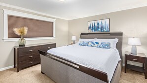 A bedroom with a bed, two nightstands, a dresser, a window with blinds, and a ceiling light.