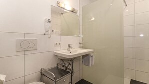 Een moderne badkamer met een witte wastafel, een spiegel, een haardroger en een douche.