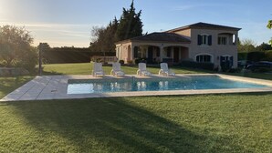 A house with a swimming pool, white lounge chairs, and a well-maintained lawn.