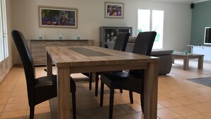 A dining area with a wooden table and chairs, a kitchen in the background, and artwork on the walls.