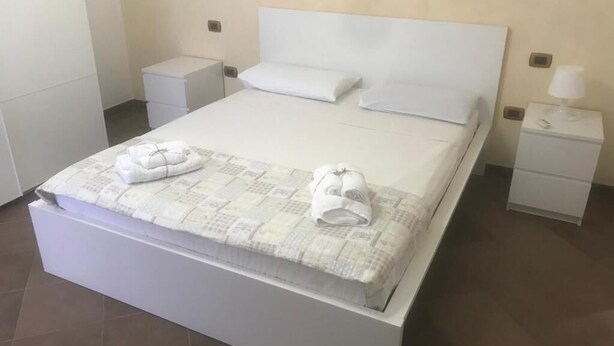 Una cama bien hecha con dos toallas, una mesita de noche y una lámpara.