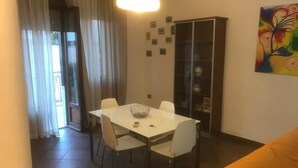 Un comedor con una mesa y sillas blancas, un aparador de vidrio y un cuadro colorido en la pared.