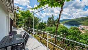 A balcony with a table and chairs, overlooking a vineyard and a coastal view.