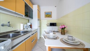 A compact kitchen with a sink, stove, and microwave. There is a dining table with plates and cups, and a vase with flowers.