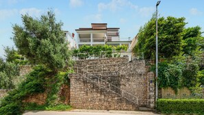 A stone staircase leading to a modern building with balconies, surrounded by lush greenery.
