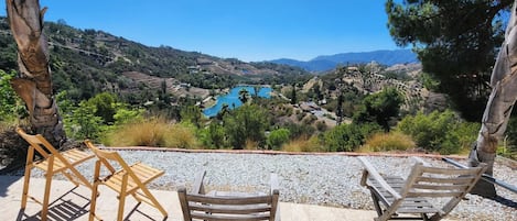 Una terraza con dos sillas de madera y una mesa, con vistas a un valle con campos escalonados y un lago azul.