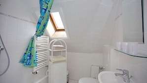 Une salle de bain avec un puits de lumière, un radiateur blanc, une étagère en verre où sont rangés les articles de toilette et un lavabo blanc.