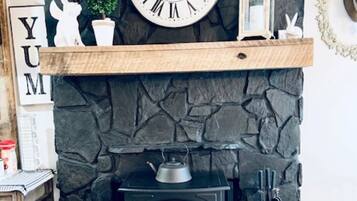 A stone fireplace with a clock above it, a small shelf with decorative items, and a wood pallet box labeled 'WOOD PALLETS' below.