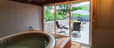 A room with a large bathtub, a stone wall, and a patio area with outdoor furniture.