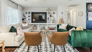 Una sala de estar con un sofá, dos sillones, un televisor y una estantería.