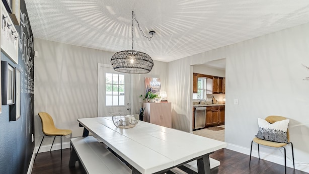 Un comedor amplio con una mesa y bancos blancos, una lámpara colgante y vistas a la cocina.