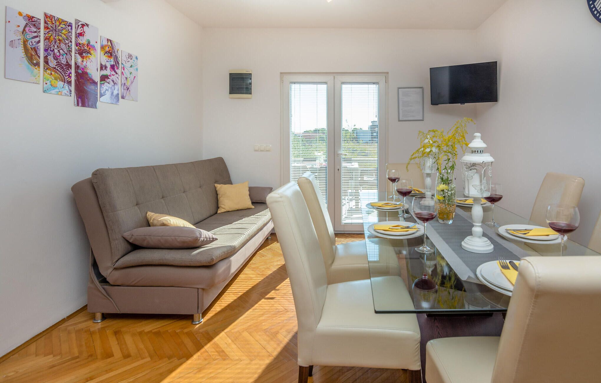 Un salon moderne avec un canapé, une table à manger pour deux personnes et un téléviseur fixé au mur.